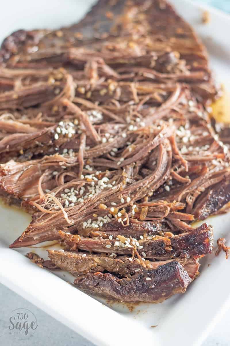 Shredded beef brisket slow cooker roast on a white plate with sesame seeds