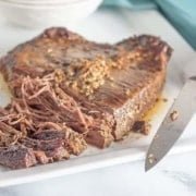 partially shredded beef brisket slow cooker on a white plate and a blue background with a knife