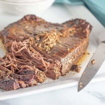 Partially shredded beef brisket slow cooker on a white plate and a blue background with a knife