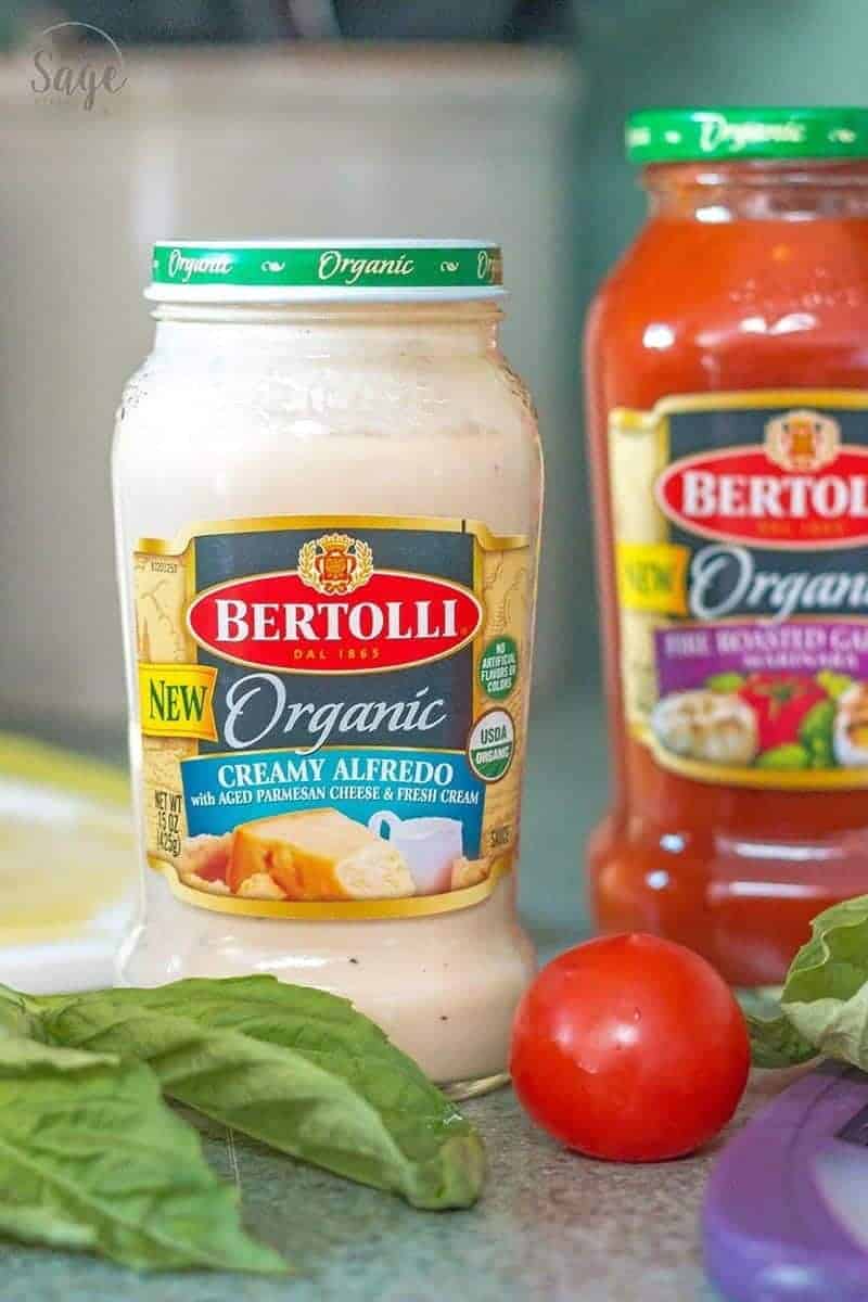 Jar of bertolli organic creamy alfredo sauce on a counter with fresh basil