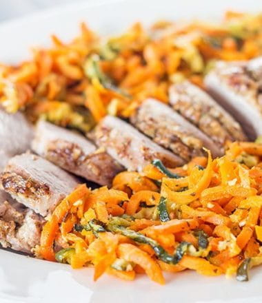 vertical photo of pork tenderloin and colorful orange spiral carrots on a white plate