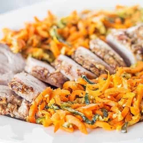 vertical photo of pork tenderloin and colorful orange spiral carrots on a white plate