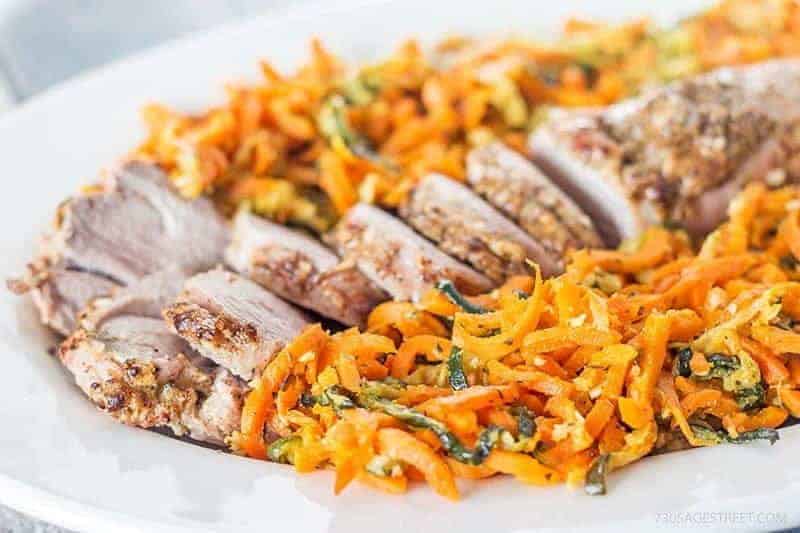 vertical photo of pork tenderloin and colorful orange spiral carrots on a white plate