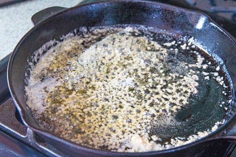 cast iron pan on a stove top with melted butter and minced garlic