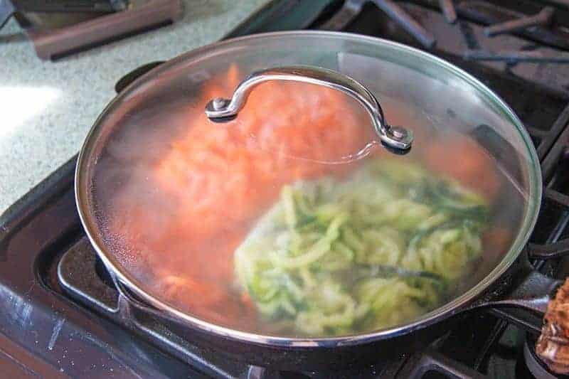 spiral carrots and zucchini in a cast iron pan with a glass lid on top