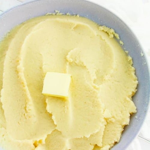 top view of mashed cauliflower in a grey bowl with a pat of butter
