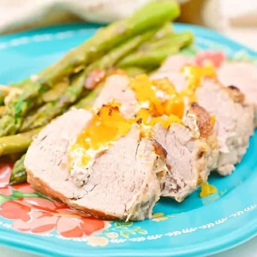 stuffed pork tenderloin on a blue plate with a side of asparagus