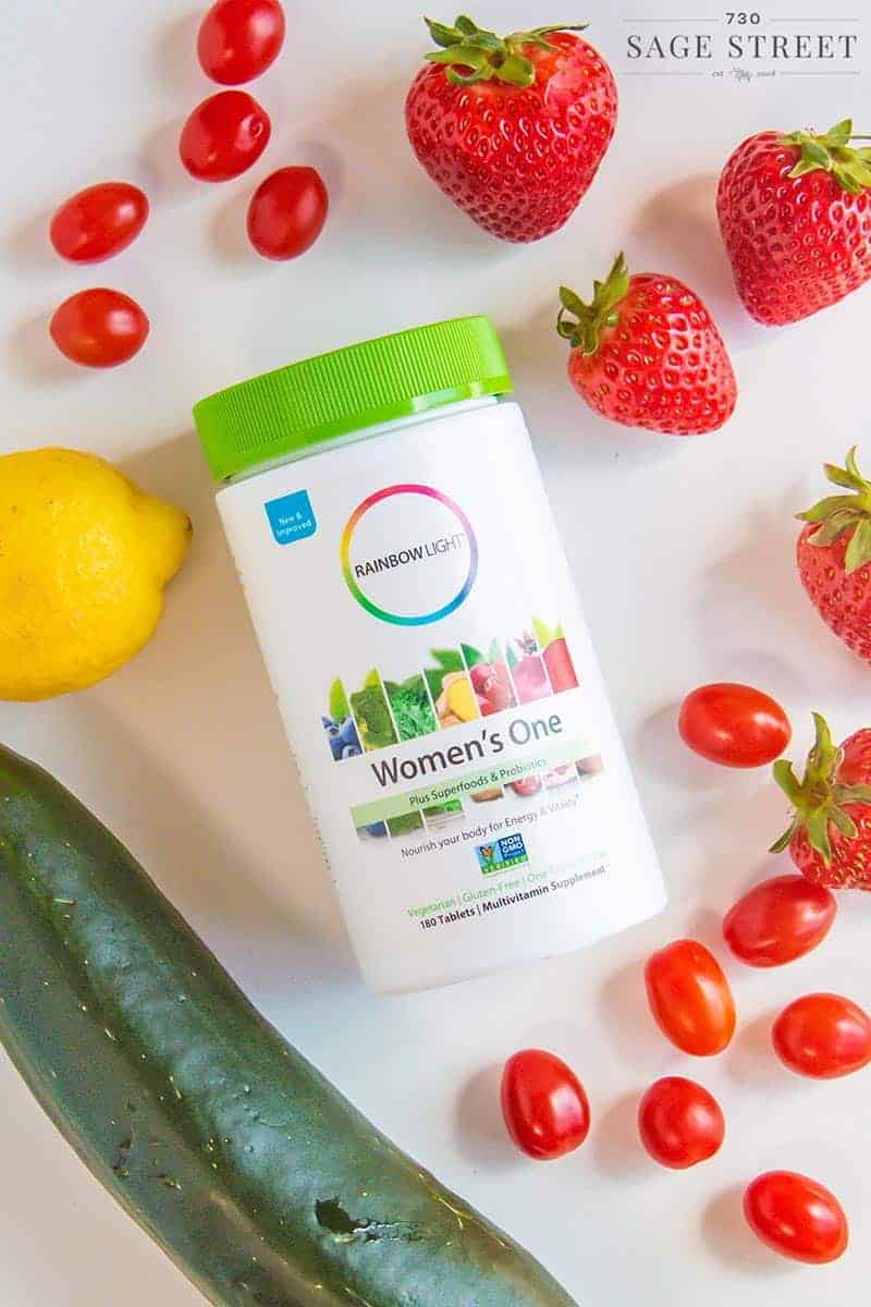 Rainbow Light Women's One multivitamin bottle surrounded by fresh fruits and vegetables
