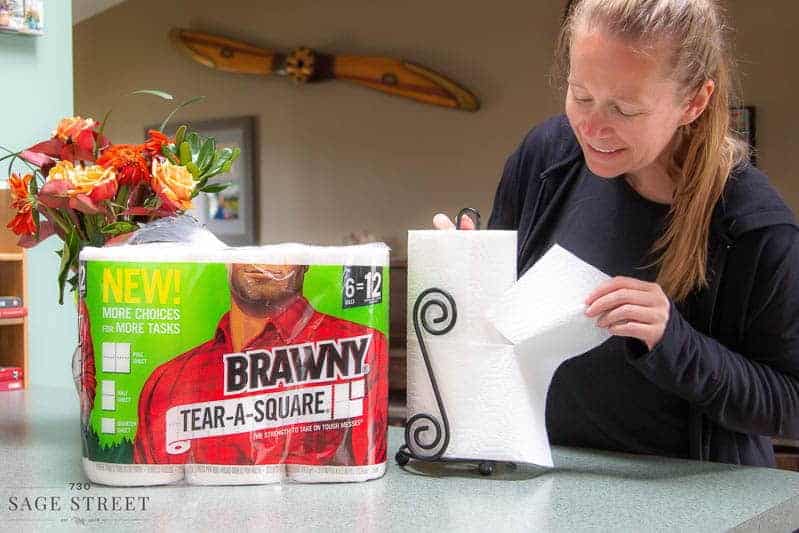 woman tearing a quarter sheet of paper towel off a roll of Brawny Tear-A-Square paper towels.