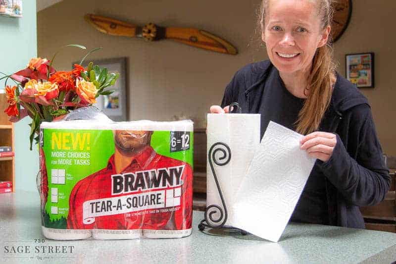 woman tearing a half sheet of paper towel off a roll of Brawny Tear-A-Square paper towels.