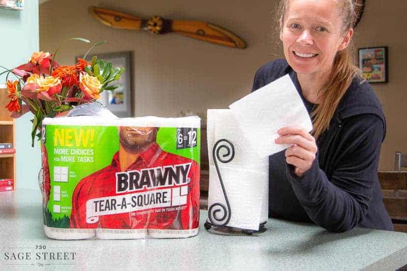smiling woman tearing a quarter sheet of paper towel off a roll of Brawny Tear-A-Square paper towels.