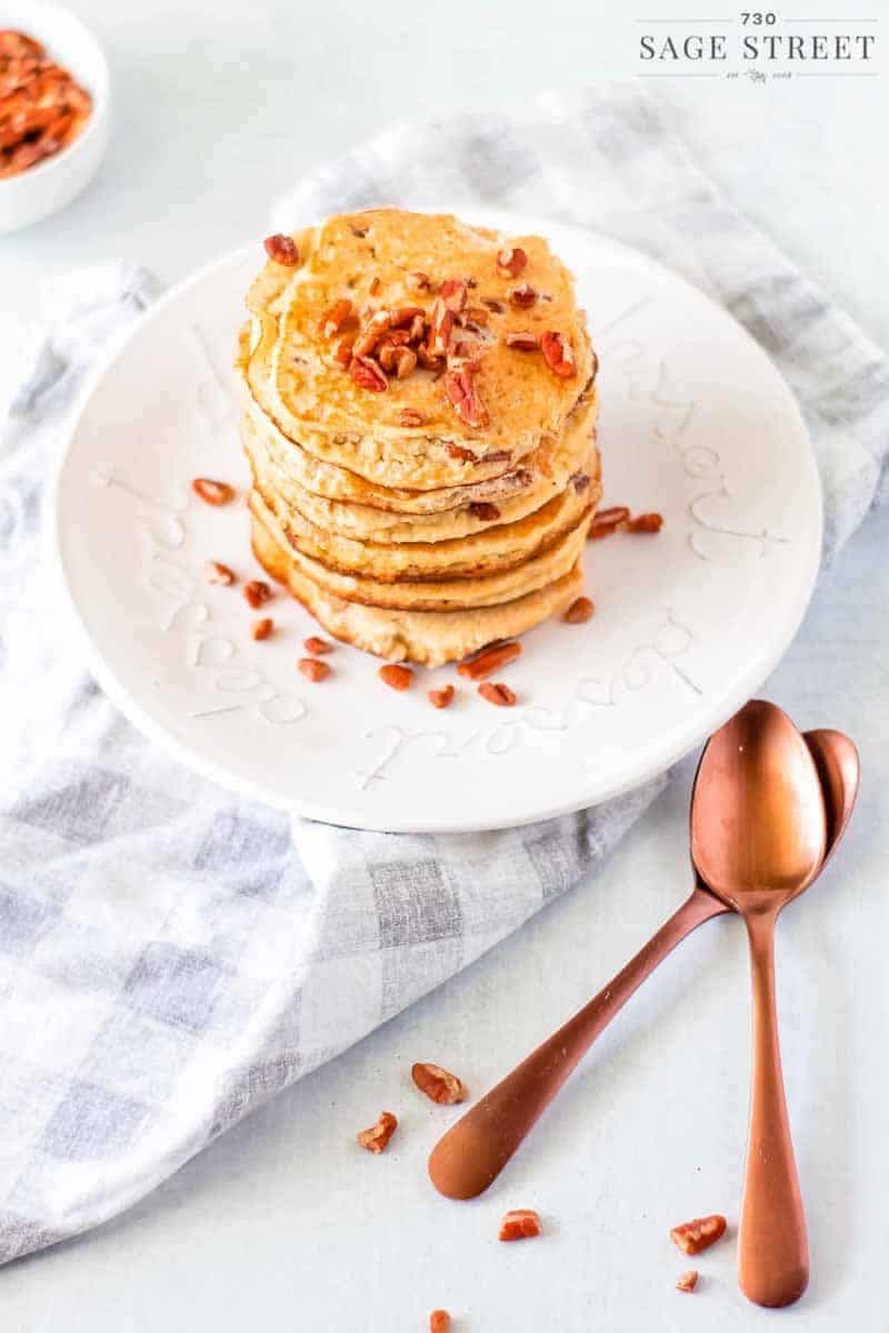 side view of keto pancakes made with ricotta cheese on a white plate sprinkled with pecans with copper spoons