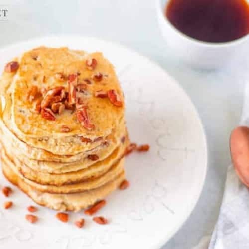 keto pancakes made with ricotta cheese on a white plate sprinkled with pecans and copper spoons next to it