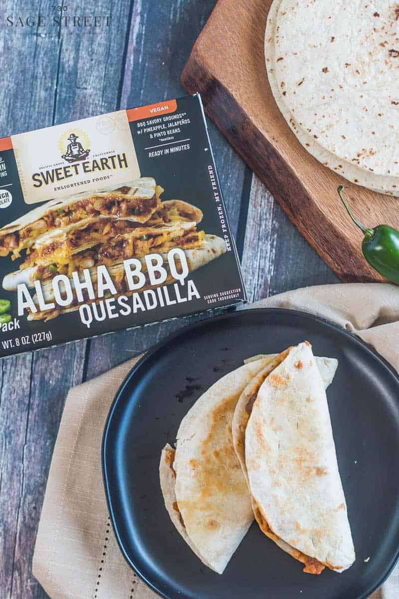 Sweet Earth Foods Aloha BBQ quesadilla on a black plate next to the product packaging
