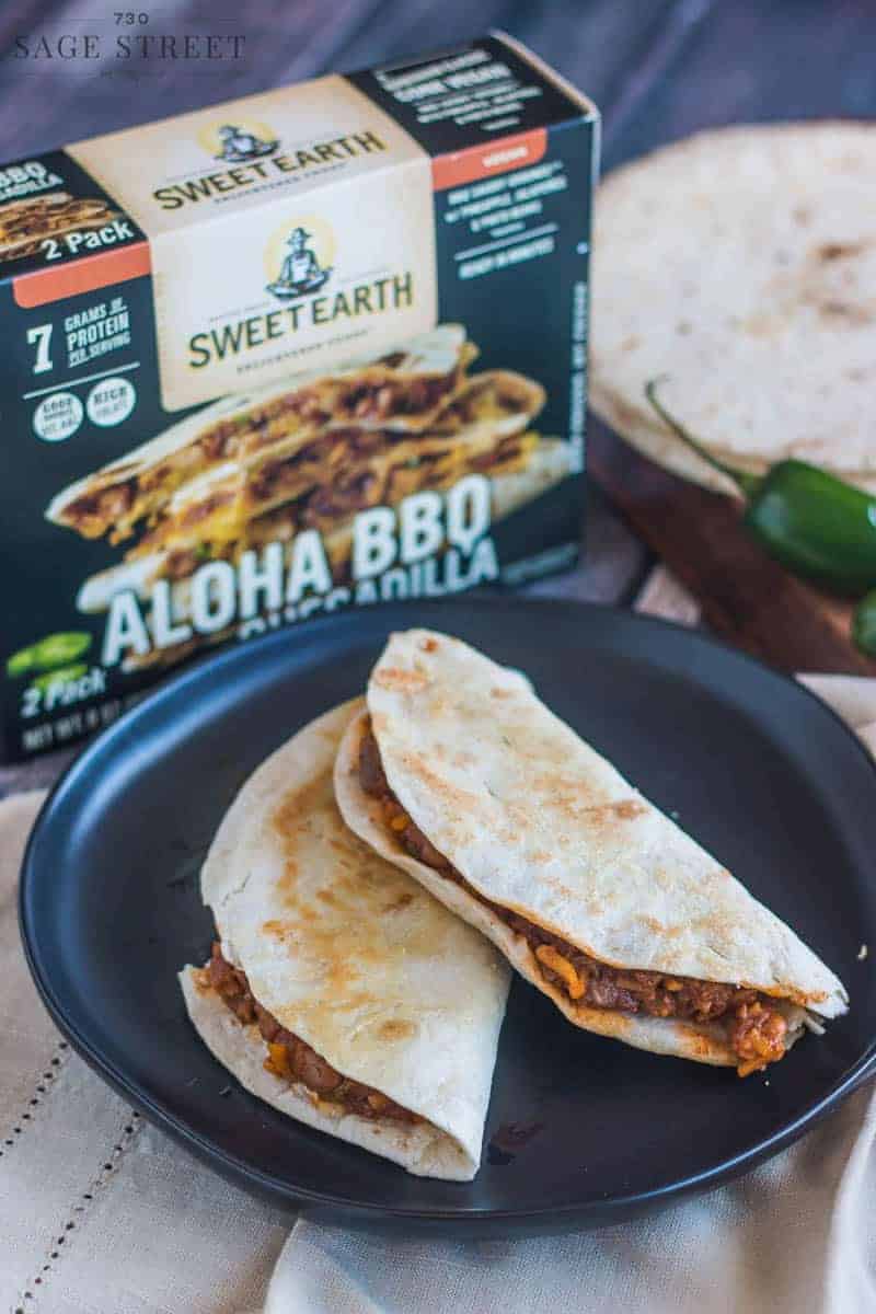 Sweet Earth Foods Aloha BBQ quesadilla on a black plate next to the product packaging