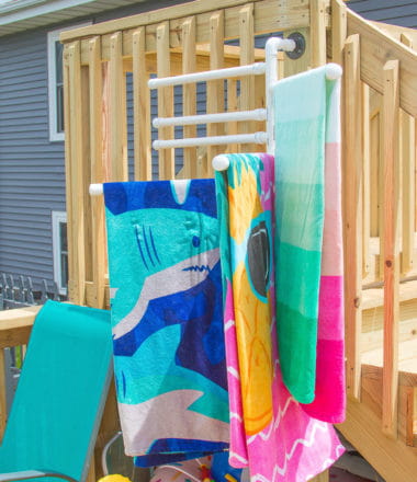 DIY pool towel rack hanging on a deck with colorful towels on it
