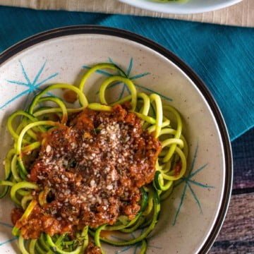 Final plate of zucchini spirals topped with bolognese sauce in a bowl viewed from the top down.