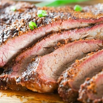 Smoked Tri-tip sliced and topped with spring onion layered on a wood cutting board. This 3 lb tri-tip cut was smoked for 3 hours on a Traeger pellet smoker.