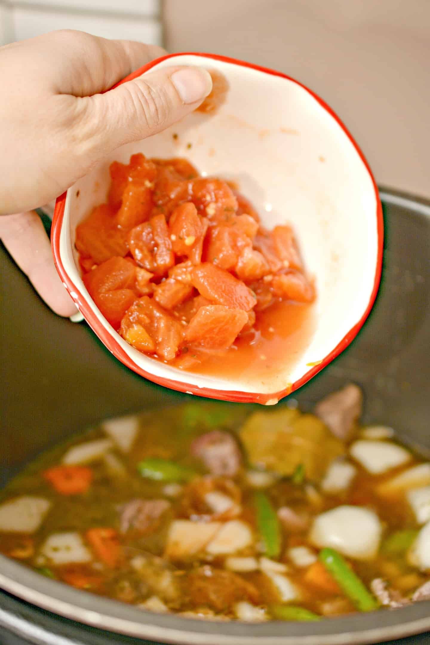 pouring diced tomatoes to an instant pot beef stew witn vegetables