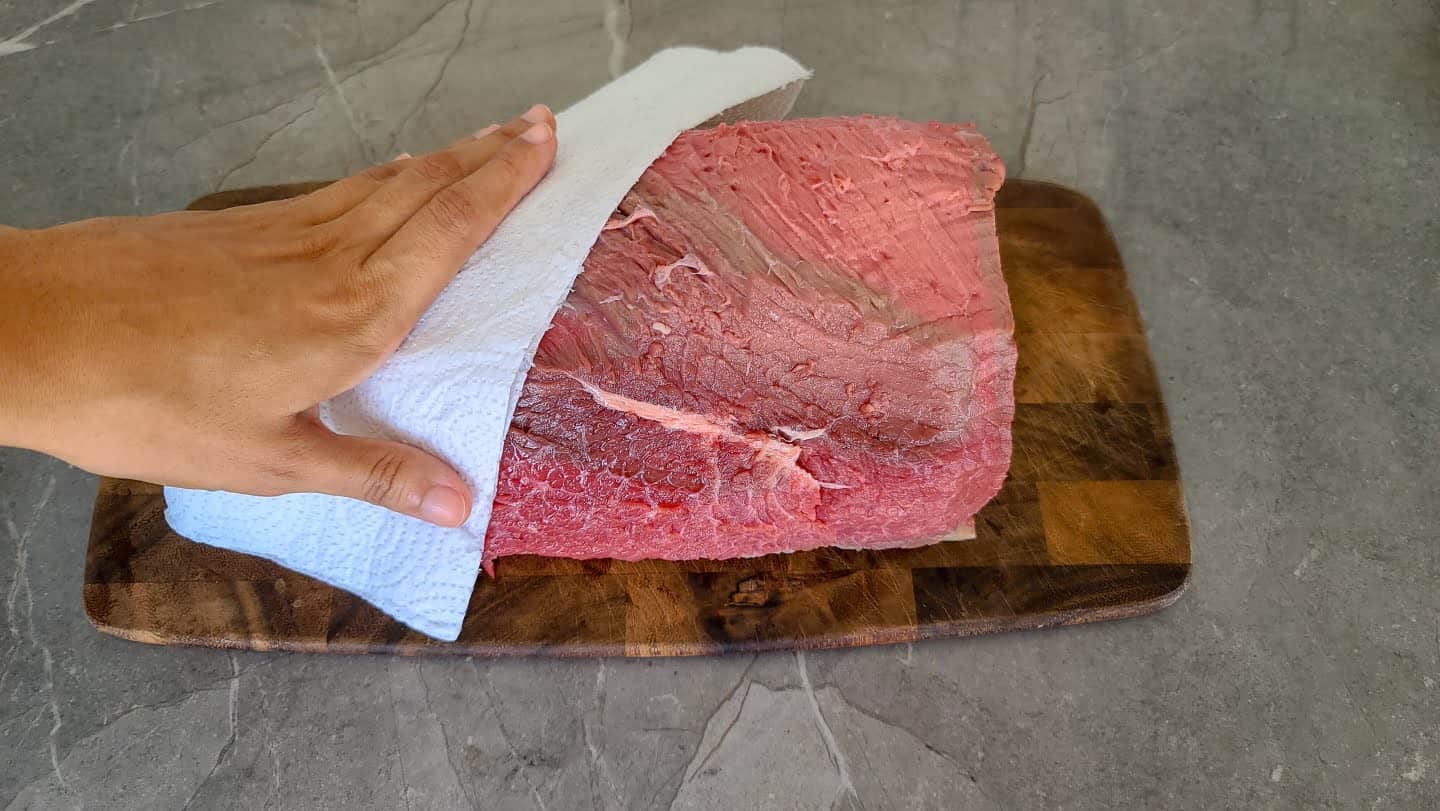 Pat dry to remove moisture from your bottom round roast. Patting roast with paper towel to absorb moisture.