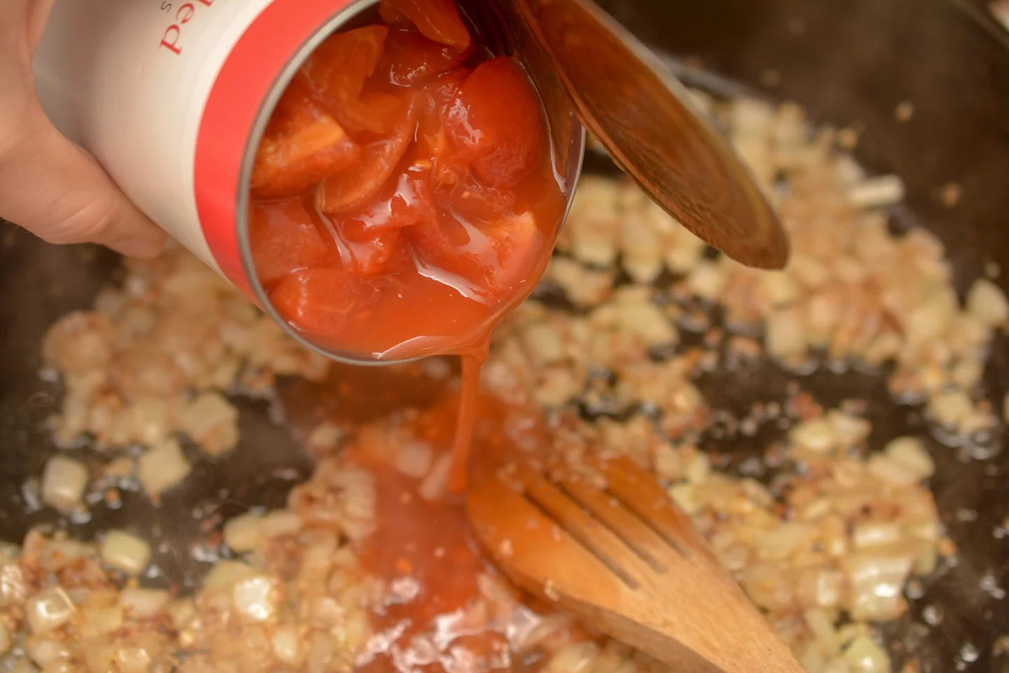 dumping can of tomatoes into butter chicken sauce