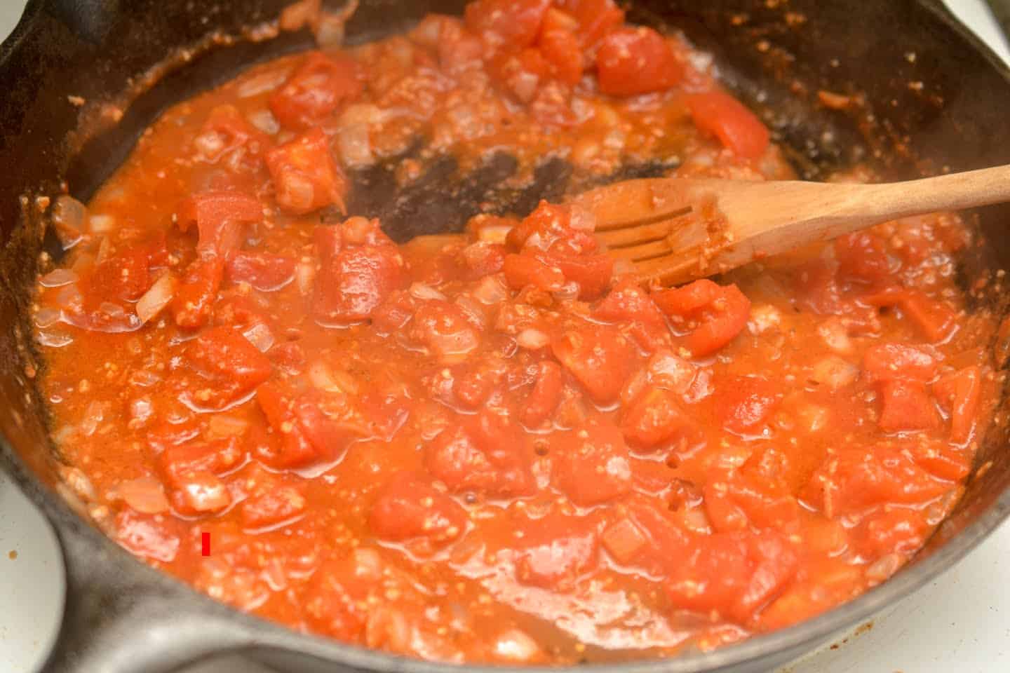 stirring butter chicken sauce with wooden spoon