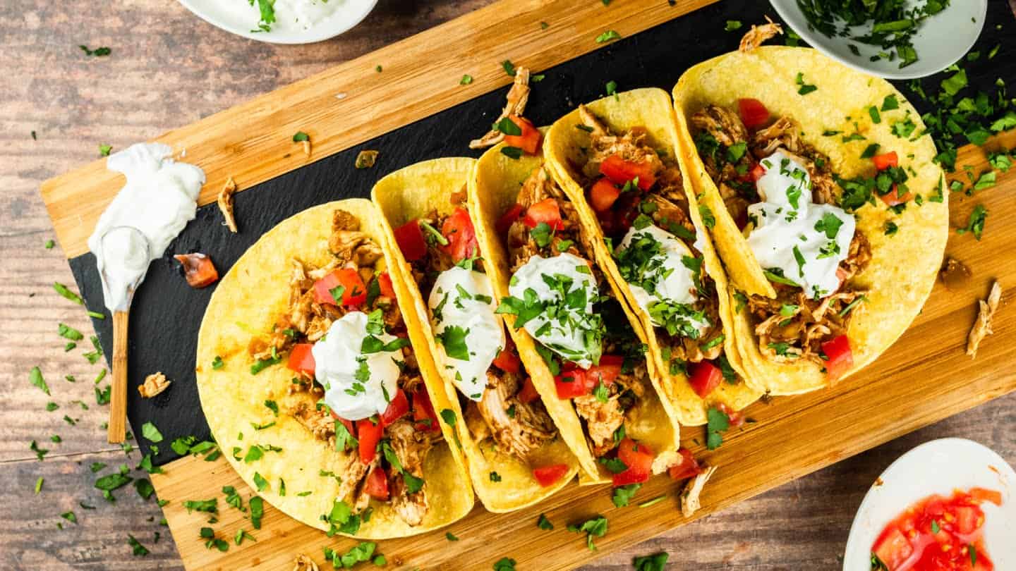 five shredded chicken tacos with sour cream and cilantro tomatoes on top