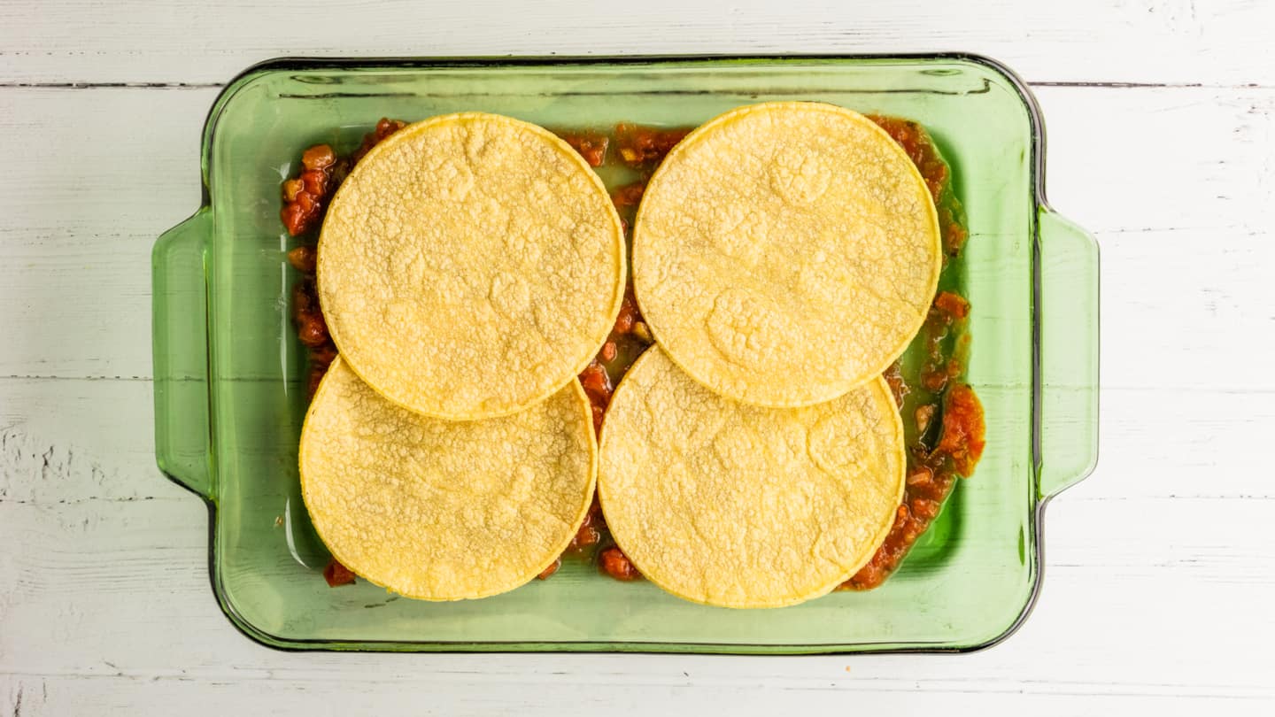 Pour the remaining salsa into a prepared baking dish and cover it with a layer of 4 corn tortillas.